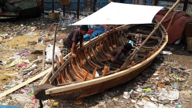 Shah Alam fixes a boat on a mound of trash next to the Buriganga river.
