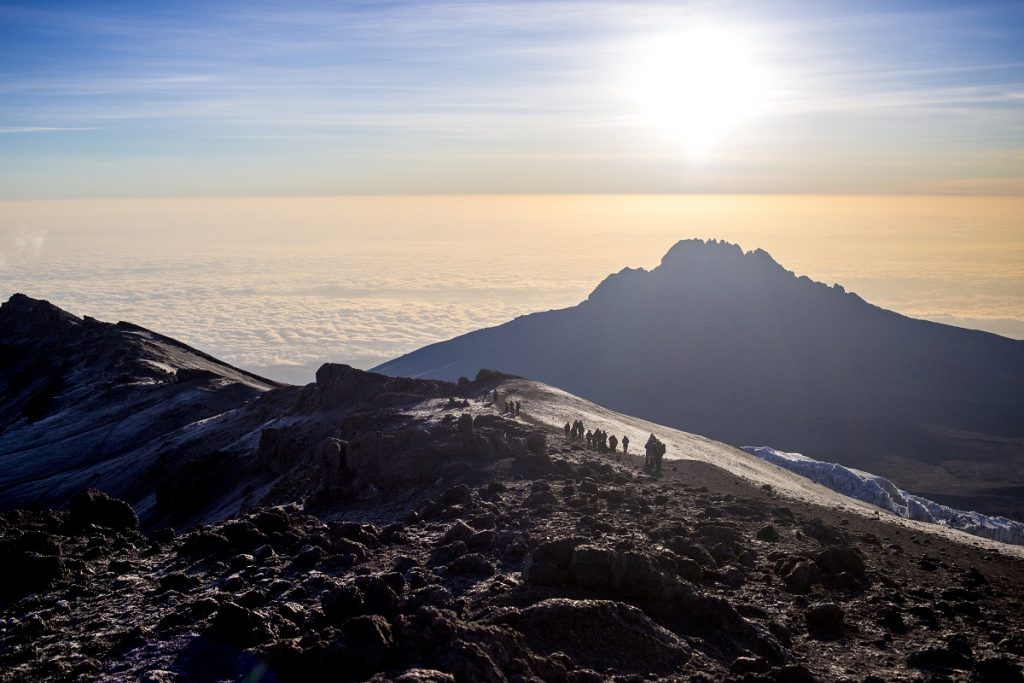 View from peak of Mt. Kilimanjaro in Tanzania, sun rising on the horizon. A group of local women farmers are descending the mountain.