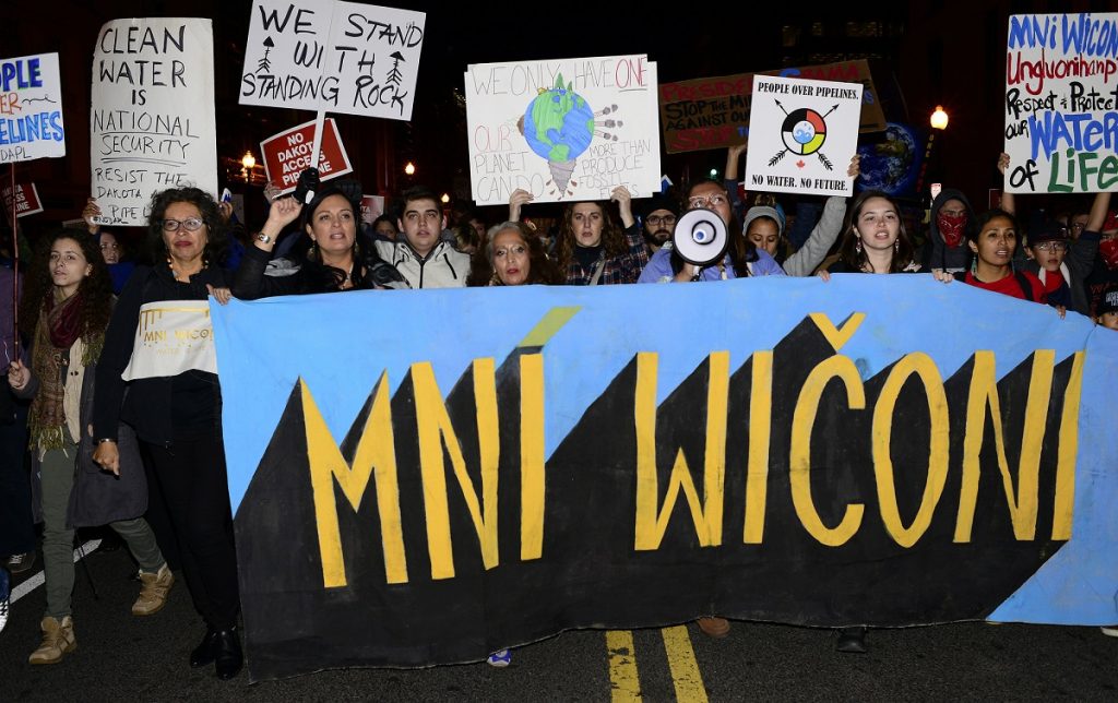 A group of protesters hold up signs along with a banner that says Mni Wiconi, which means Water Is Life in the Lakota language, spoken by the people of the Standing Rock Sioux Tribe.