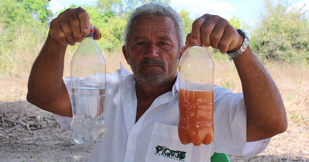 A villager in northeastern Brazil holds two plastic bottles, one filled with waters polluted by agribusiness activity