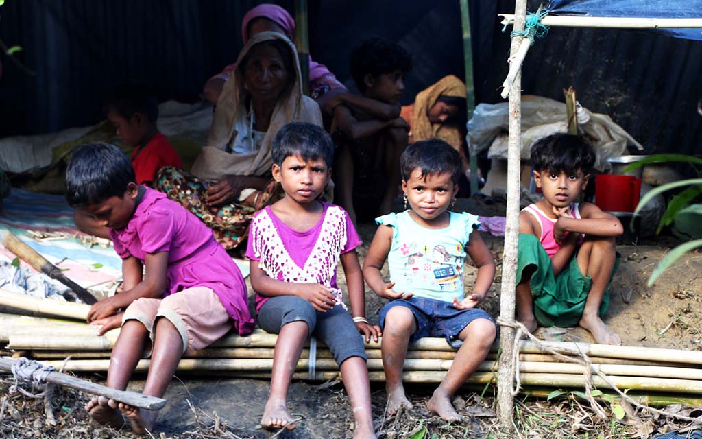 Four Rohingya children sit under a tent at a refugee camp in Bangladesh.