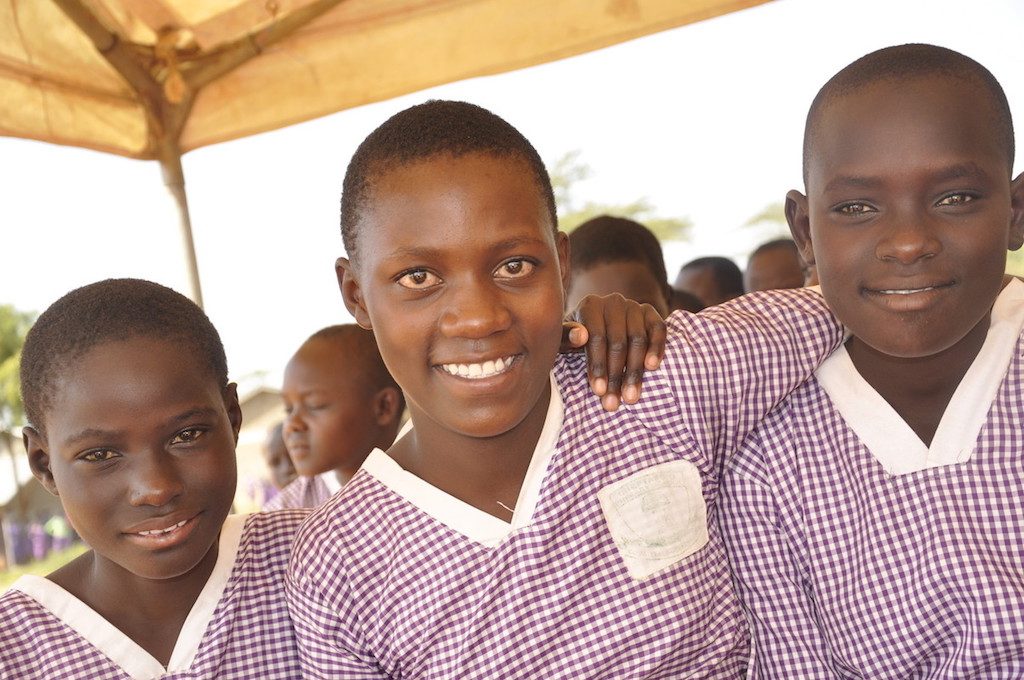 Three young women smile with their arms on each other's shoulders.