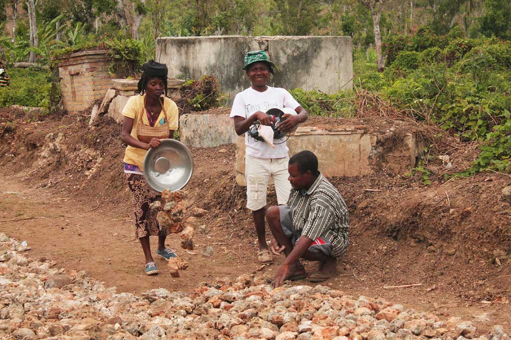 In Haiti, two women and a man place stones on the ground as they repair roads after Hurricane Matthew.