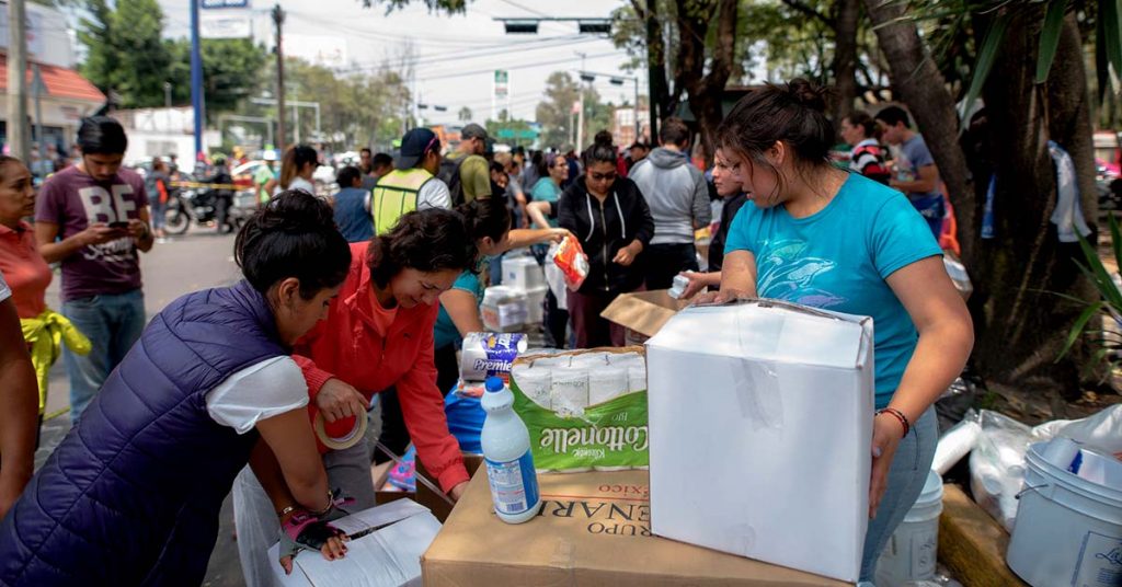 Two women are taping up a box of provisions for survivors of an earthquake in Mexico in September 2017. A woman to their right is moving another box of provisions.