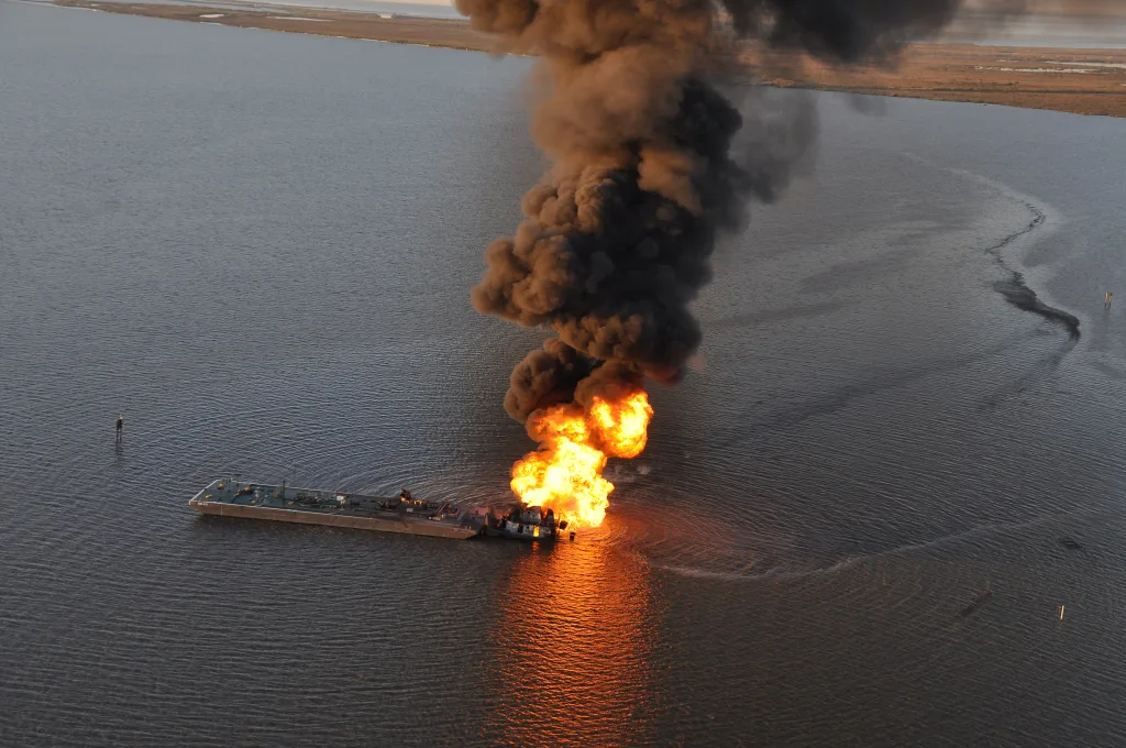 Dark smoke rises from a tug boat in a large body of water. This is an example of why some Louisianans oppose the Bayou Bridge Pipeline.