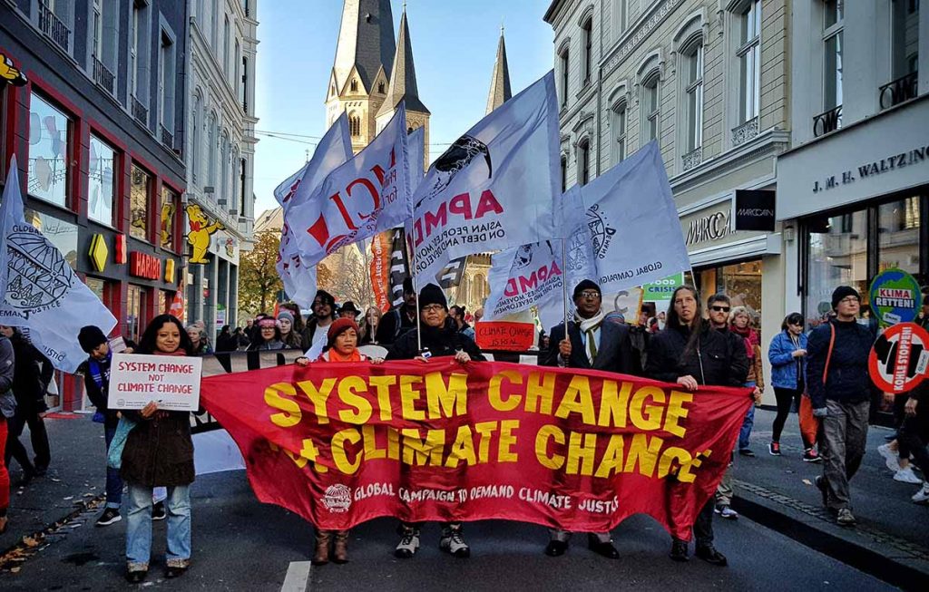 Climate activists at the 2017 UN climate negotiations march down a street in Bonn, Germany, holding a banner that says "SYSTEM CHANGE NOT CLIMATE CHANGE".
