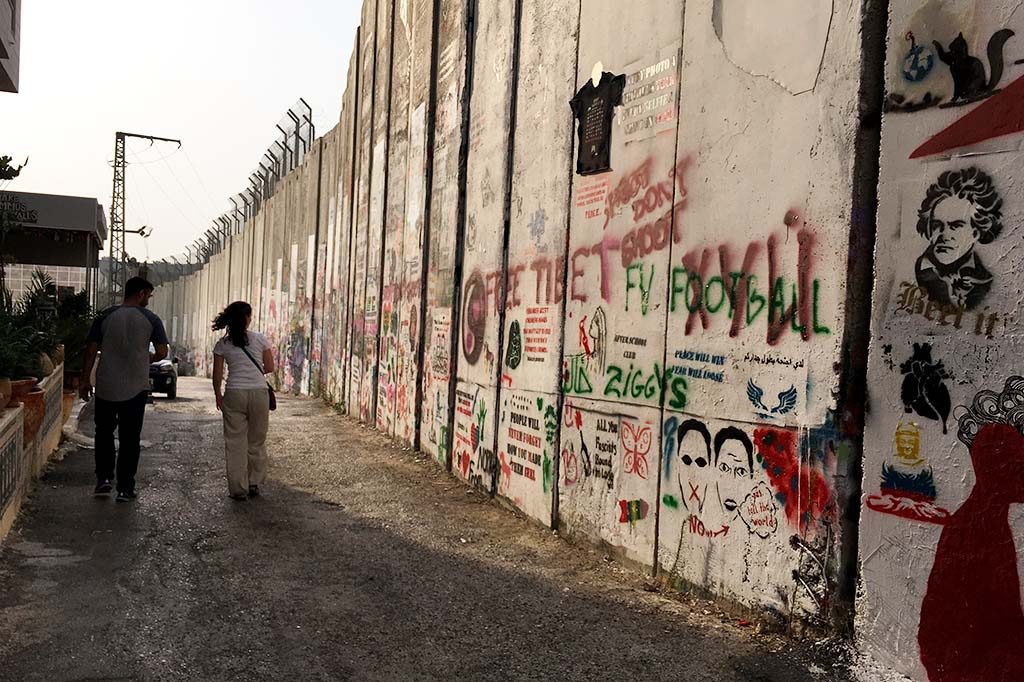 A man and a woman walk alongside a section of the separation wall in Bethlehem, West Bank, outside Banksy's Walled Off Hotel.