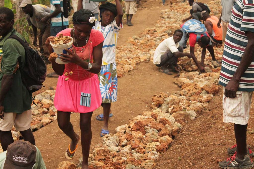 A woman in Haiti carries a bucket of rocks to rebuild a road after Hurricane Matthew.