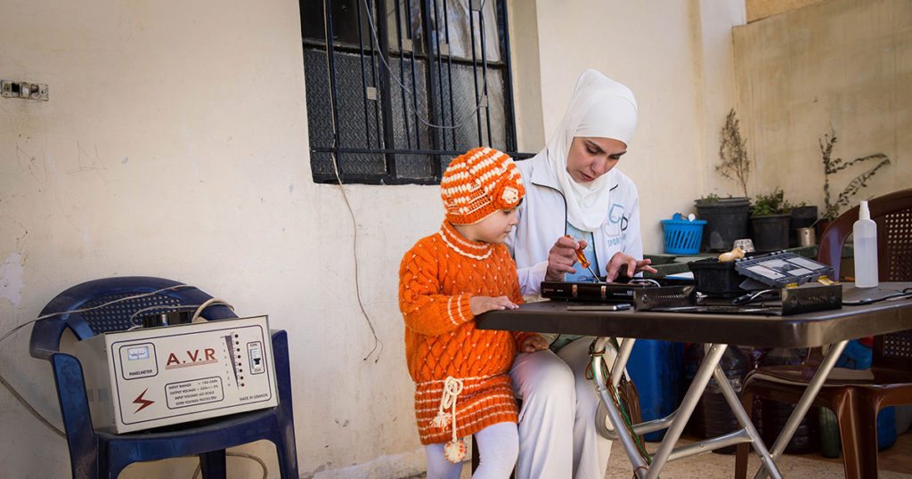 A Syrian refugee woman fixes an electronic gadget while her niece sits next to her, watching. They fled civil war in Syria, which has produced the largest refugee crisis since WWII.