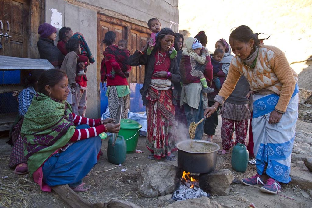 A group of women and children congregate around a large pot of stew cooking over rocks. They participated in the Nepal Agriculture Food Security Project.