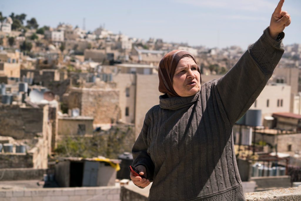 A Palestinian woman wearing a hijab points upward.