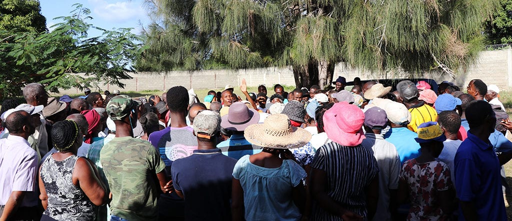 A group of Haitian farmers gather in an outdoor space to discuss the details of the final agreement.