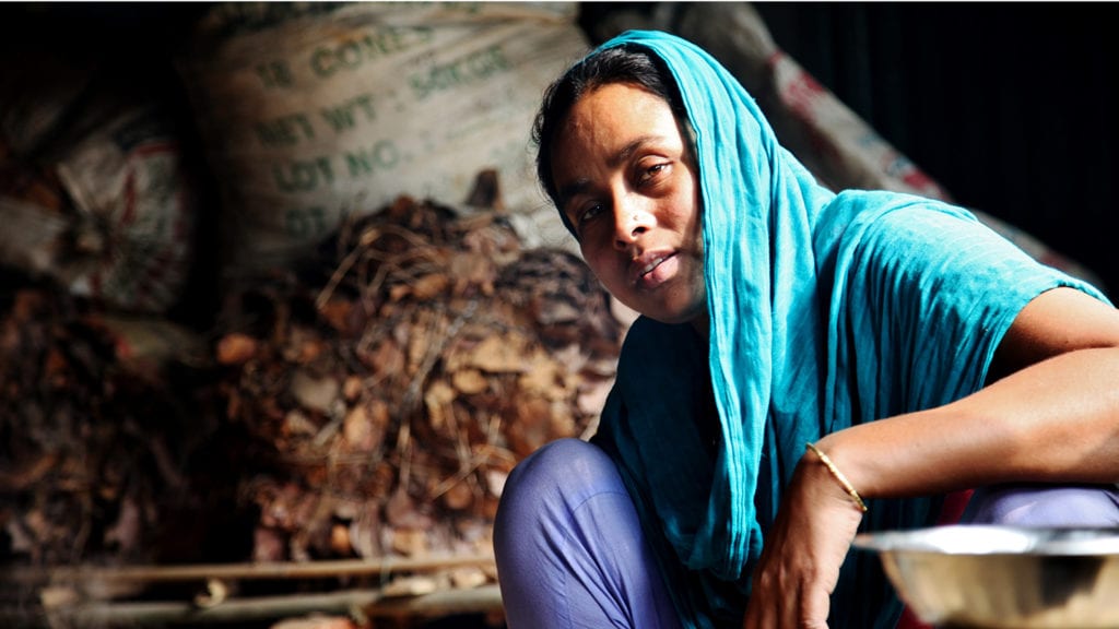 A Bangladeshi woman with a scarf sits, looking down at the camera.