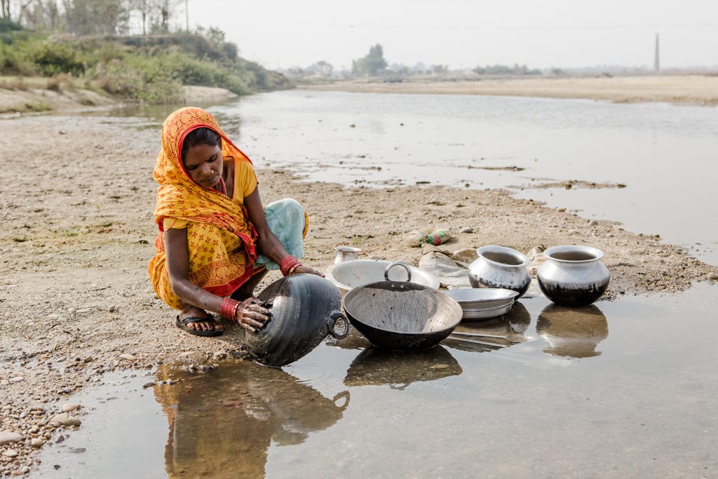 A Nepali woman squatting near a pool of water to wash pots and pans.