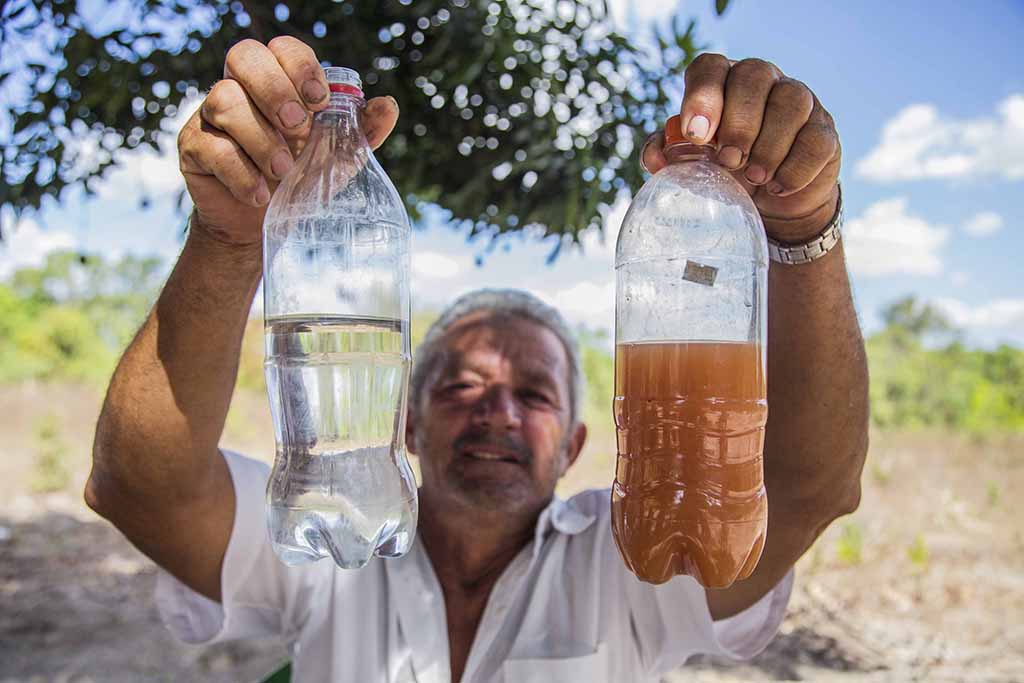 A man holding up two water bottles, one with clear water and one with water polluted by agribusiness runoff, in Brazil.