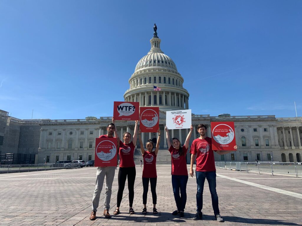 Five young people in red, ActionAid-branded T-shirts stand in front of the U.S. Capitol Building holding signs with messages for climate action