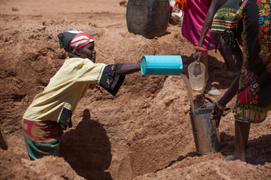 A woman standing in a ditch pours water into a bucket.